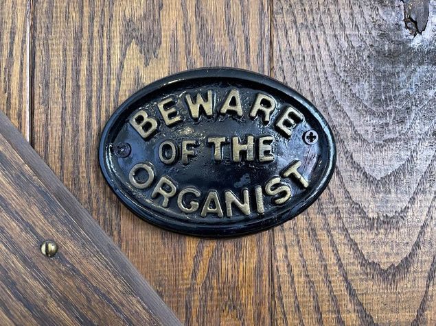 The humor in this door sign (photo) derives from the fact that keeping one's distance from certain things is actually a warning to organists, not their visitors.
We allude here to such concerns as distractions.
The subconscious mind is the seat of memory, and it will function automatically for us in a performance situation if fear is taken out of the way.
It's important therefore for us to focus down on what's happening in the current measure of music as we play, concentrate, and NOT let things distract us -- like a sudden, unexpected, enormously loud and startling burst of patriotic applause -- like maybe some tricky place up ahead -- like some earlier mistakes we had to correct or one that crops up unexpectedly -- like someone asking us questions -- like someone wanting to shake hands with us --  like someone wanting us to look into their camera and smile while we're trying to sight read from the page (yes, they do that to us, too).
All of these things can trip us up by hijacking our eyes, ears, hands, mind, and/or attention; while we're smoothly cruising along in a performance situation these kinds of things can suddenly grab our focus, our concentration, by the scruff of the neck and rudely strip it away for a moment, leaving nothing behind but our motor memory and the task of recovering our bearings.
No tension -- no play -- but relaxation needs to be blended in so that it's about a 50:50 mix of tension and relaxation -- what amounts to getting in the middle of the road and never all of one thing; in that sense, being able to balance one against the other at any point along the way makes organ playing very athletic.
What many of our well-meaning non-musician friends and listeners don't always seem to realize is that a stream of inspired sound doesn't simply emerge from the instrument by some automatic process as soon as organists seat themselves at the bench and start playing; the musician's total attention, mind, memory, and focus are needed to where, with the possible exception of receiving a smile and a nod of the head, it's impossible to hold any semblance of meaningful communication with them at the same time.
From a purely mechanical standpoint there are no issues (save for physical limitations) which repetition, having the right tools, and adopting the habit of fiercely concentrating cannot solve.
To be alert enough to concentrate requires us to guard our health and get enough rest; here again, it's all about balance.
Everything in organ playing is balance [See blog, Balance In Organ Playing, Parts I-III].
When we play, if we make a little mistake, we don't dwell upon it -- we just leave it behind and keep moving forward ... it's in the past.
If we begin to start thinking about why we just made the mistake then pretty soon we're making a few more because we're getting distracted and not staying with the moment.
It can be aggravating when we know we can play it better and have done so countless times -- interference can enter the mind from any direction -- but we just need to chalk it up, forget about it, and keep moving, just like we would when we're sight reading.
The more we can cultivate the habit of NOT getting provoked with ourselves if a little blemish happens in our playing, the better our memory will function through the remainder of the music.
Some of the best advice we can receive is to let go of that perfection thing ... to forget about playing it 